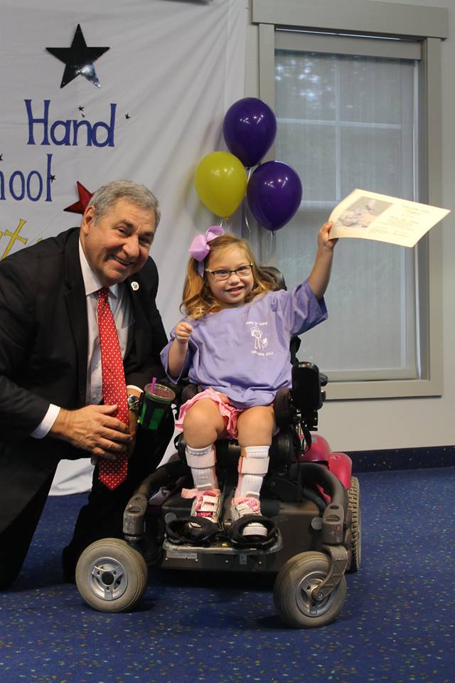 Young girl in wheel chair holding up a certificate