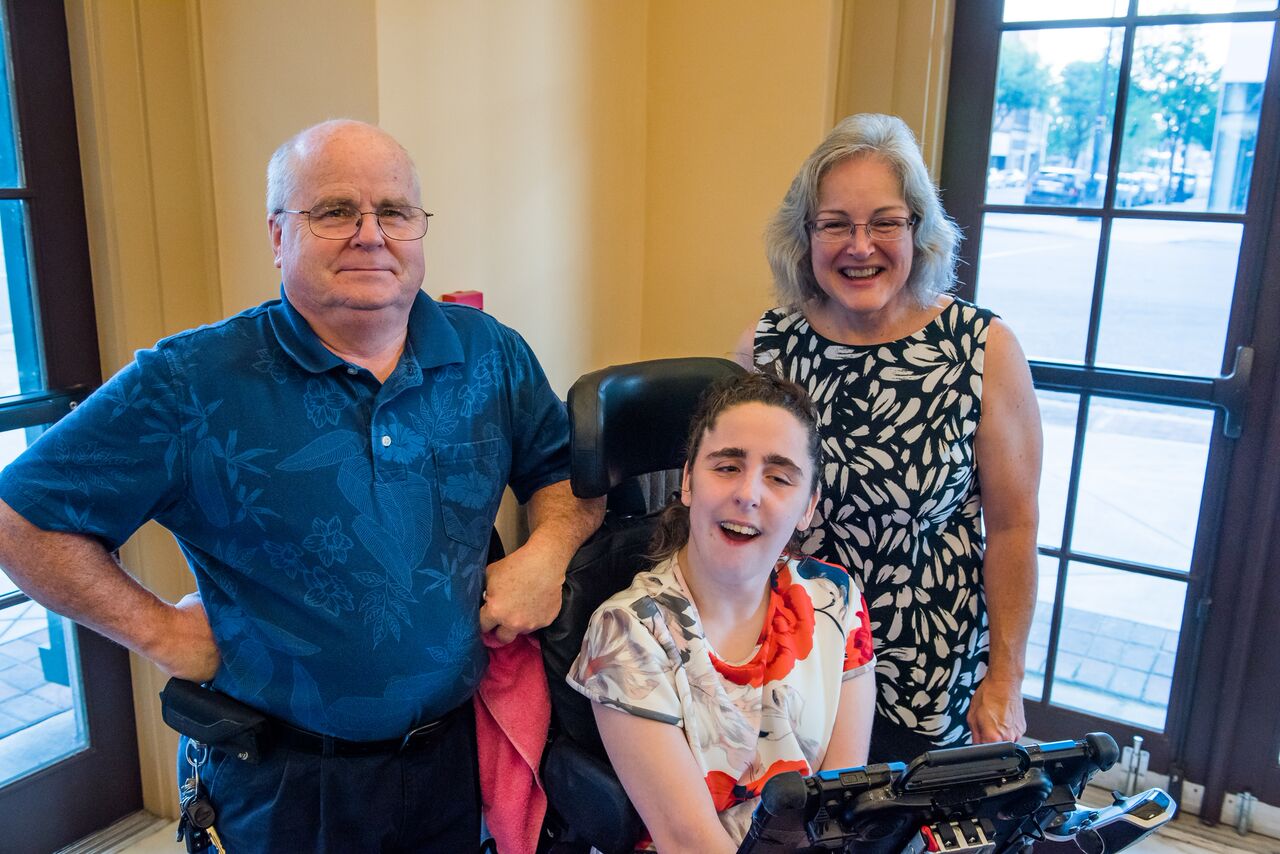 Young girl in wheel chair smiling with her parents